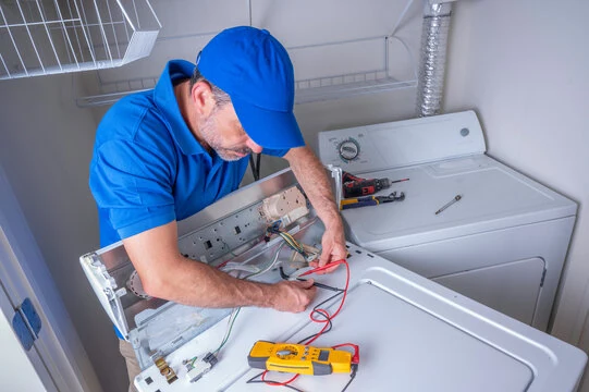 Repair technician testing a laundry appliance control panel with a meter
