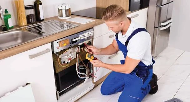 Technician examining wiring and controls on a built-in kitchen oven